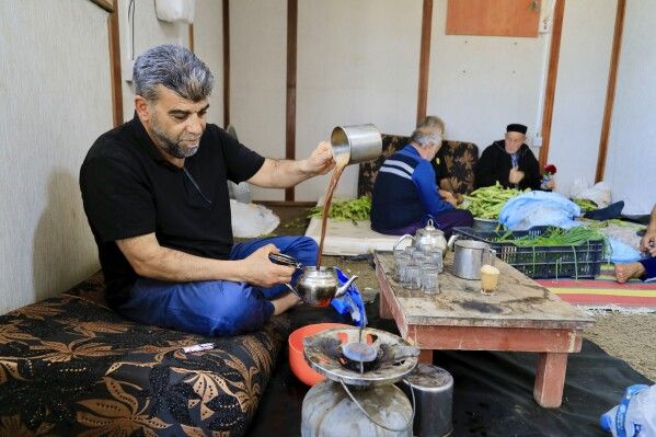 A man serves tea as volunteers prepare Bazin, a traditional Libyan dough bread made of barley or whole wheat flour and often served with stew in Tajoura, east of Libya's capital Tripoli, Tuesday, March 11, 2025, during the Muslim holy month of Ramadan. (AP Photo/Yousef Murad)